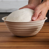 A baker’s hands lifting dough from a boule banneton.