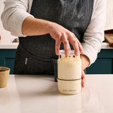 A baker lifting a Starter Jar lid with stretchy, matured sourdough starter.