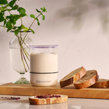 Risen sourdough starter in a small Starter Jar alongside slices of sourdough bread and fresh mint in a glass vase on a kitchen counter.